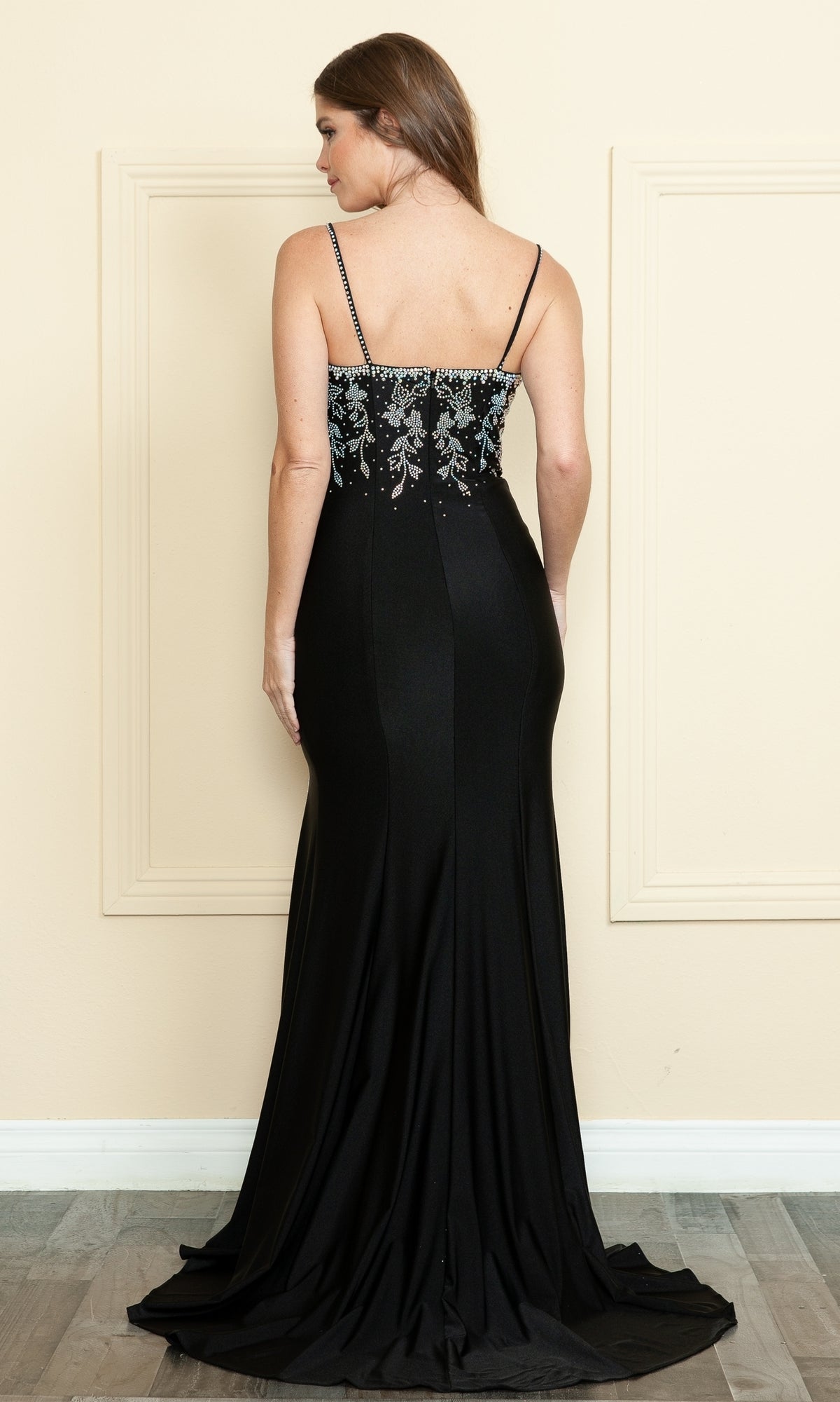 A woman wears the Beaded-Bodice Long Prom Dress (Poly USA 9122), featuring a beaded bodice and thin straps, photographed from the back indoors against a beige wall with decorative molding.